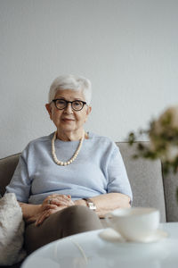 Senior woman with hands clasped sitting on sofa at home