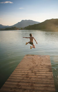 Rear view of shirtless boy jumping in lake