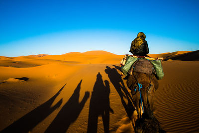 Rear view of people riding in desert against clear sky
