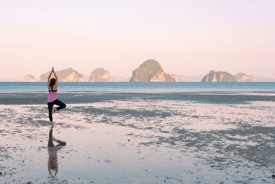 Young asian woman workout by doing yoga on the beach at sunrise