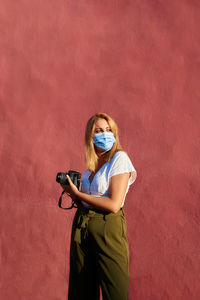 Young woman with a mask and a camera on a red background