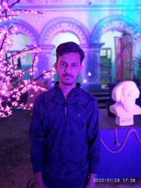 Portrait of young man standing against illuminated lights at night