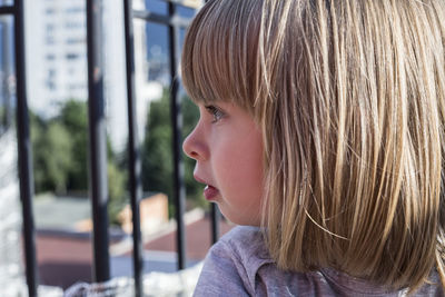 Close-up of thoughtful girl with blond hair by fence