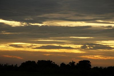 Silhouette trees against dramatic sky during sunset