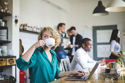 Young businesswoman drinking coffee while computer programmers working in background at office