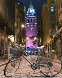 Bicycles on street amidst illuminated buildings at night