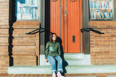 Full length portrait of smiling young woman against brick wall