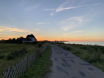 Road amidst field against sky during sunset