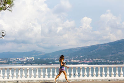 Woman standing on railing by sea against sky