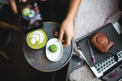 Directly above view of female blogger photographing matcha tea and snack through smart phone at creative office