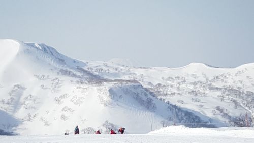 Hikers by snow covered mountains against clear sky