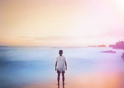 Rear view of man standing on beach against sky