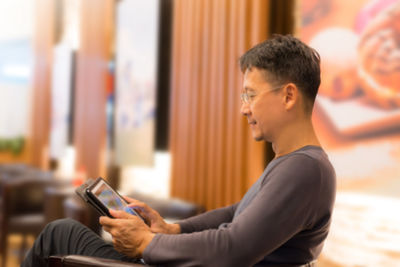 Side view of mid adult man using digital tablet while sitting on chair