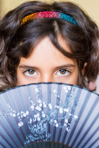 Close-up portrait of girl holding hand fan in front of face