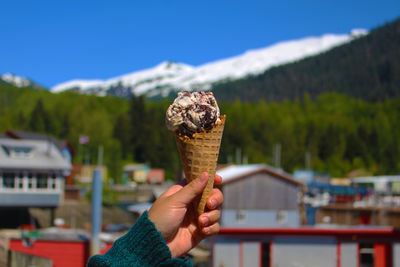 Cropped hand holding ice cream cone against mountain