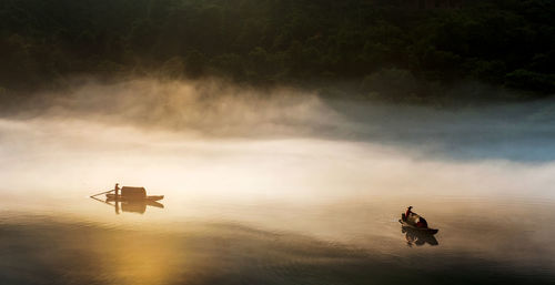 High angle view of man on boats sailing in lake during foggy weather