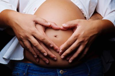 Close-up of couple's hands forming heart shape on pregnant belly