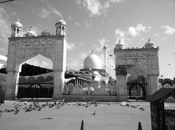 Flock of birds perching by mosque against sky