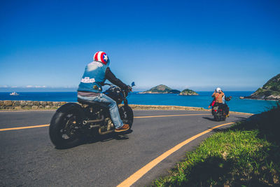 People riding motorcycle on road against clear blue sky