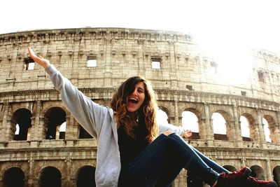 Portrait of happy woman sitting against coliseum