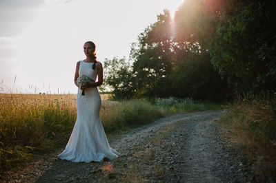 Woman standing on field by road against sky