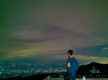 Man standing by illuminated buildings against sky during sunset