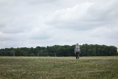 Rear view of man walking on field against sky