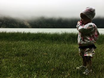 Side view of boy standing on grassy field against sky