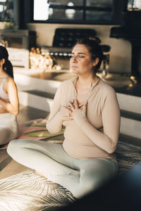 Woman meditating with hands on chest sitting cross-legged at retreat center
