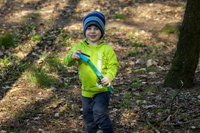 A pretty boy on a walk in the woods, wearing a blue cap blowing soap bubbles. 