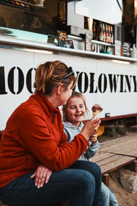 Mother and her daughter eating ice cream sitting on a step in front of food truck during vacations