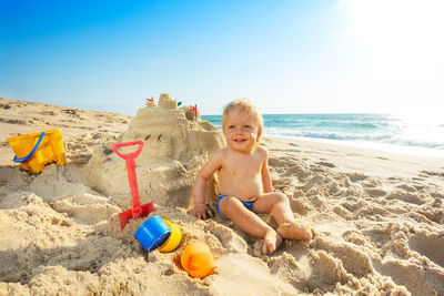 Portrait of boy playing with sand at beach against sky