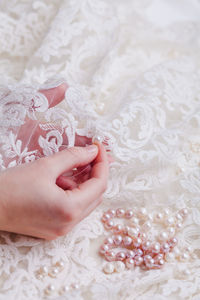 Cropped hand of woman stitching pearls on white wedding dress