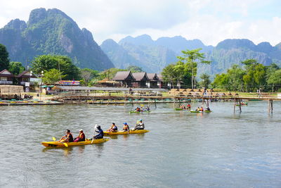 People on boats in river against mountains