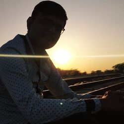 Man sitting on railroad track against sky during sunset