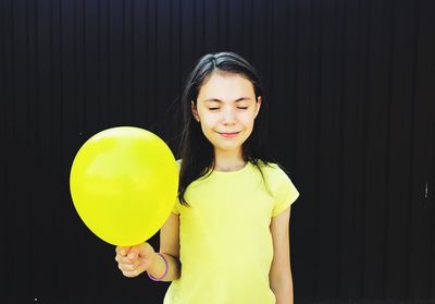 Smiling girl holding yellow balloon against black background