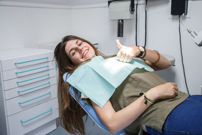 Portrait of smiling young woman showing thumbs up on dentist chair