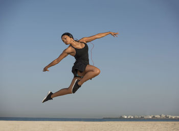 Young woman dancing at beach against clear sky