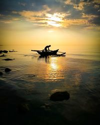 Silhouette man in boat on sea against sky during sunset