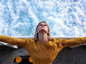 High angle view of young woman with arms outstretched standing by railing over sea