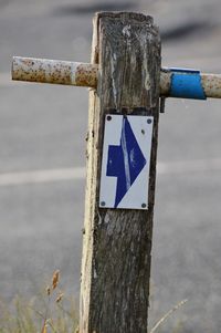 Close-up of arrow sign on wooden post on roadside