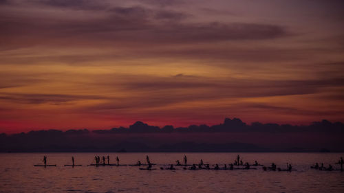 Silhouette people by sea against sky during sunset