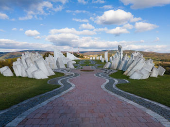 Footpath leading towards stone wall against cloudy sky