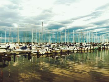 Boats moored at harbor against cloudy sky