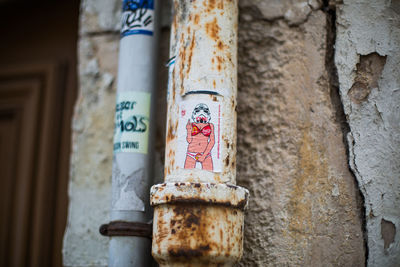 Sticker showing obscene gesture on rusty metallic pipe against wall