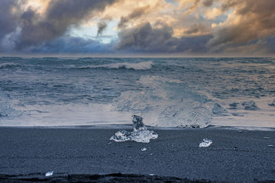 Iceberg chunk on black sand against waves rushing at diamond beach during sunset