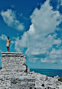 Man standing on retaining wall at beach against blue sky