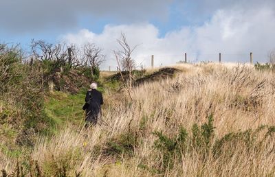 Rear view of man walking on field against sky