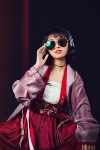 Young woman wearing sunglasses while standing against black background