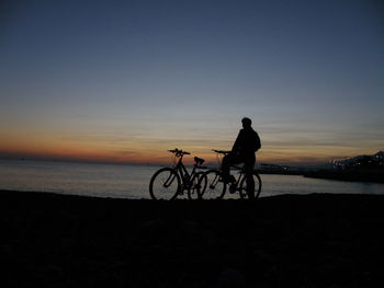 Silhouette man with bicycle at beach against sky during sunset